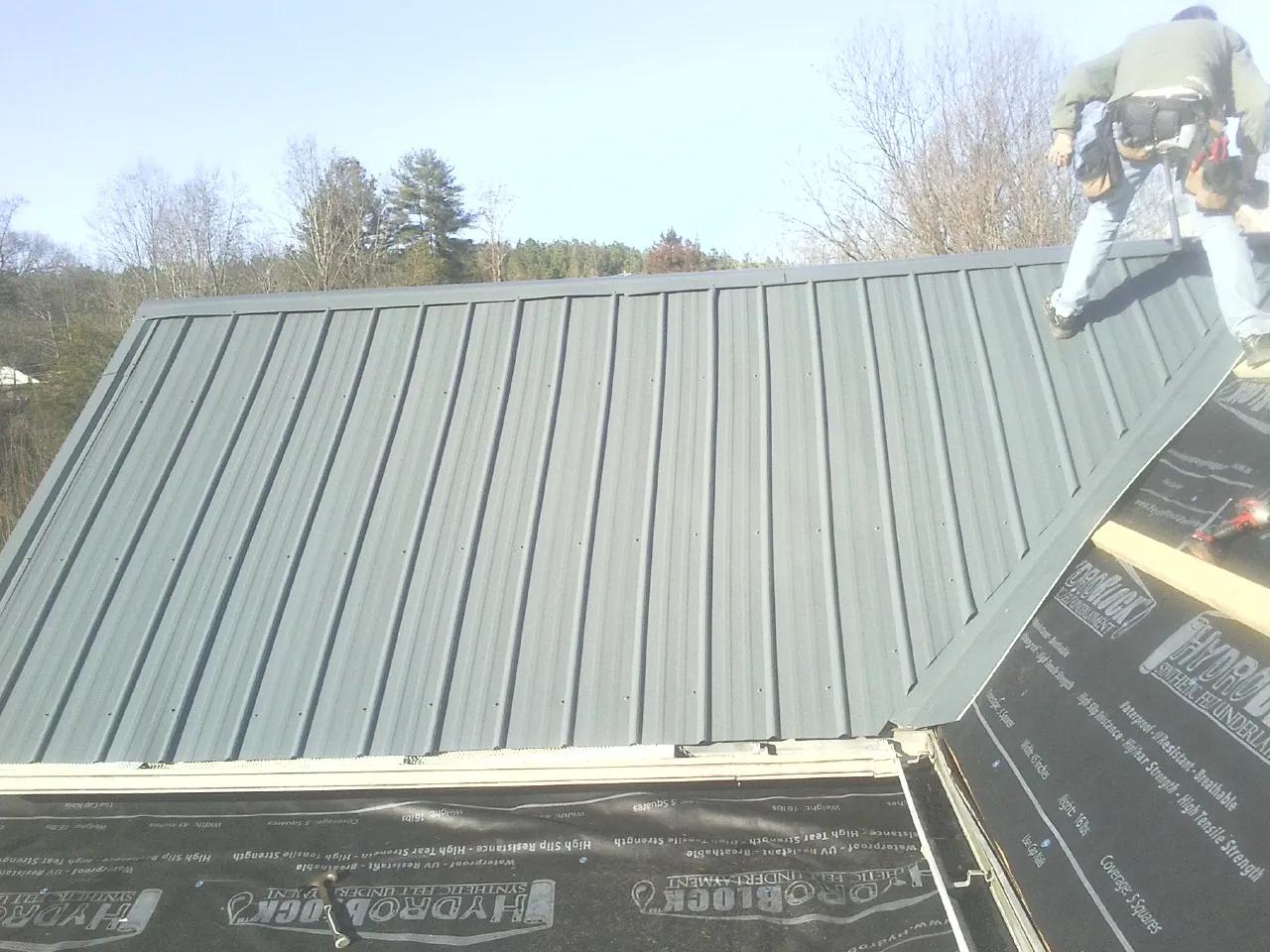 Crew installing dark green standing seam panels over synthetic underlayment in Minneapolis