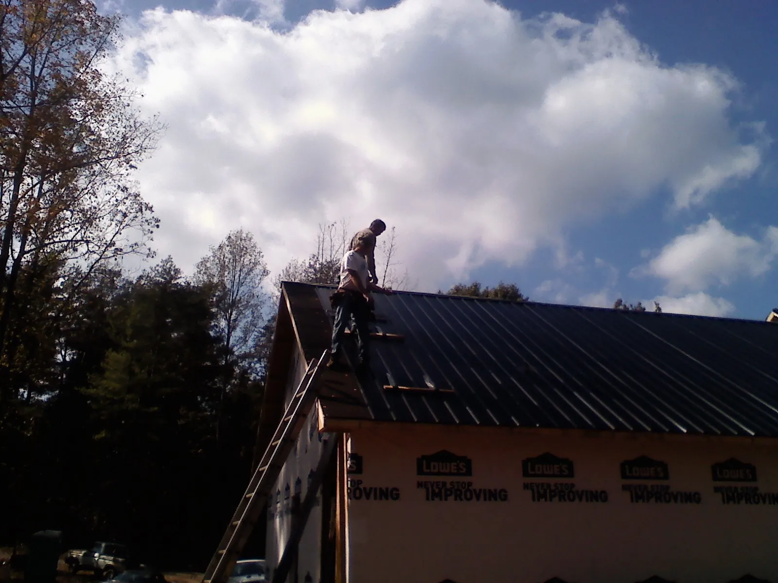 Roofer fastening dark metal panels high against a cloudy sky, from a Roof Inspection job in Minneapolis