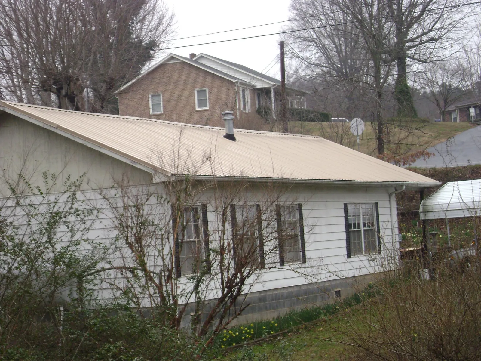Tan metal roof on a white sided house set into a hillside — Commercial Roofing by Roofing Brothers in Minneapolis